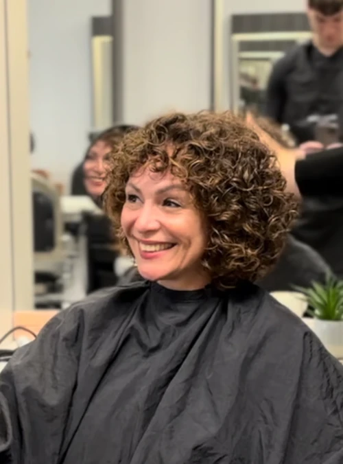 Kundin im Friseursalon mit kurzem, lockigem Bob und Friseurumhang