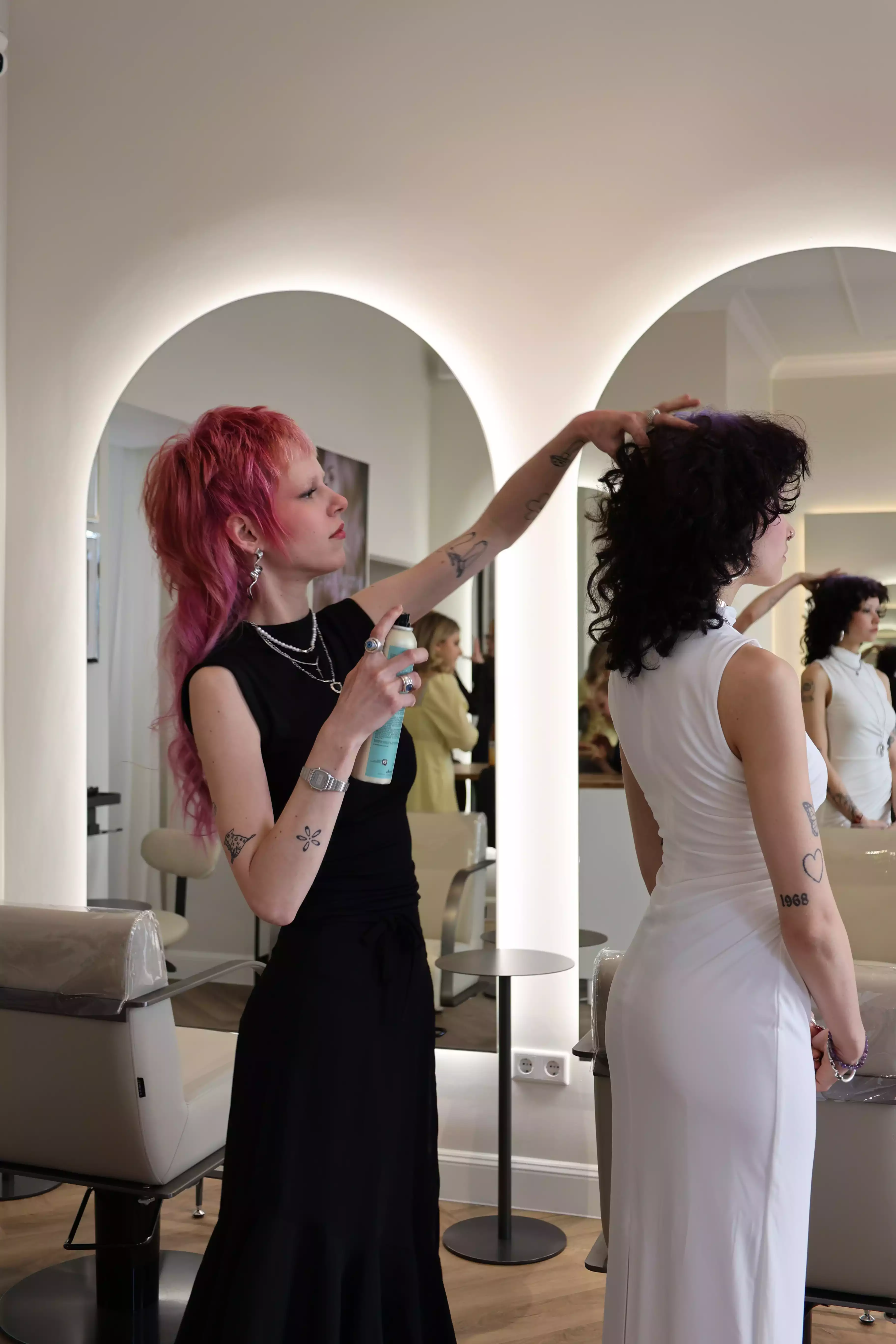 Friseurin stylt Kundin im Salon, fixiert Locken mit Haarspray am Spiegel.