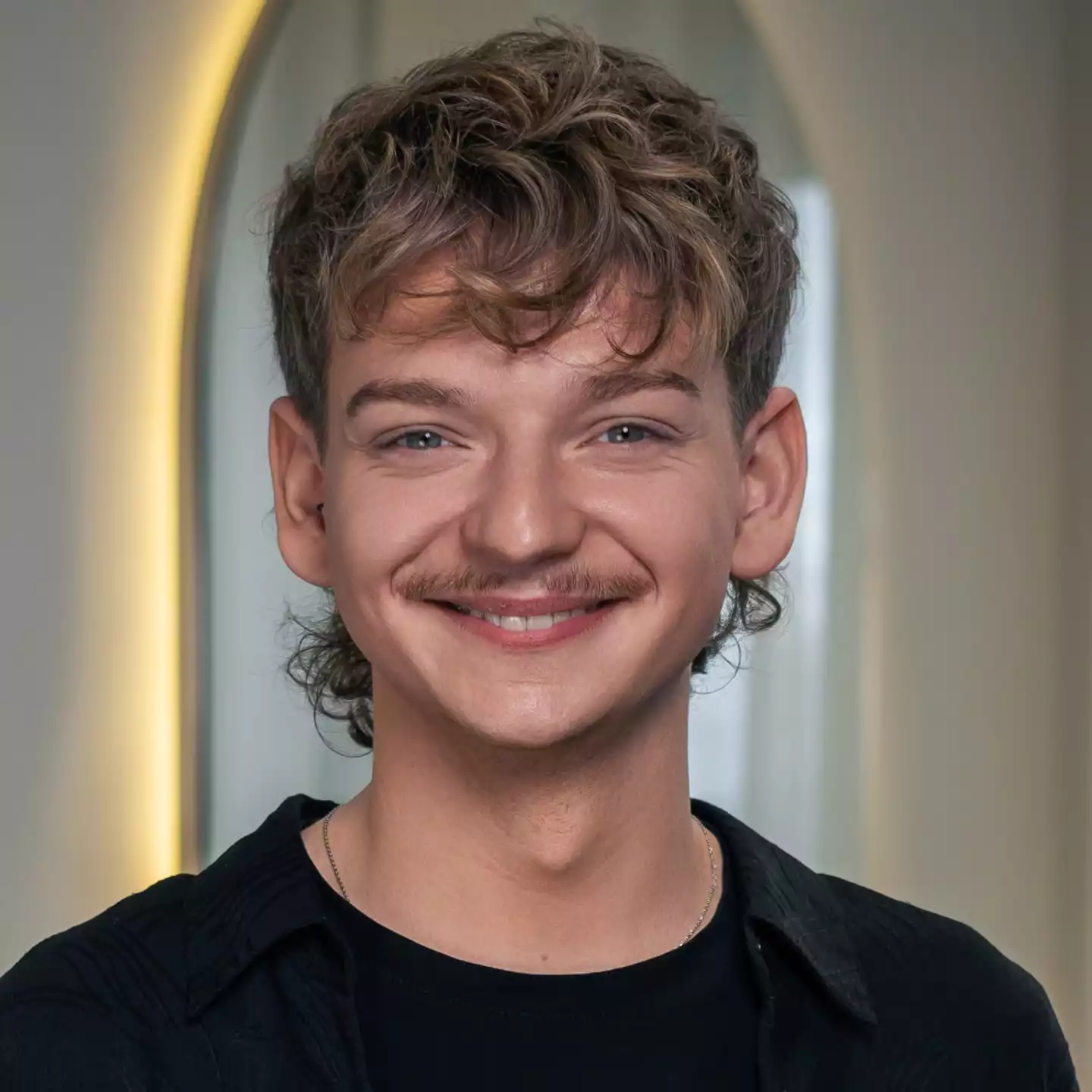 Porträt eines lächelnden Mannes mit lockigem Haar und Schnurrbart, indoor.